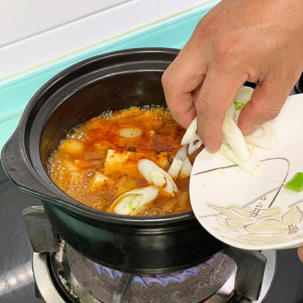 끓는 두부찌개에 풋고추와 대파를 넣는 모습.