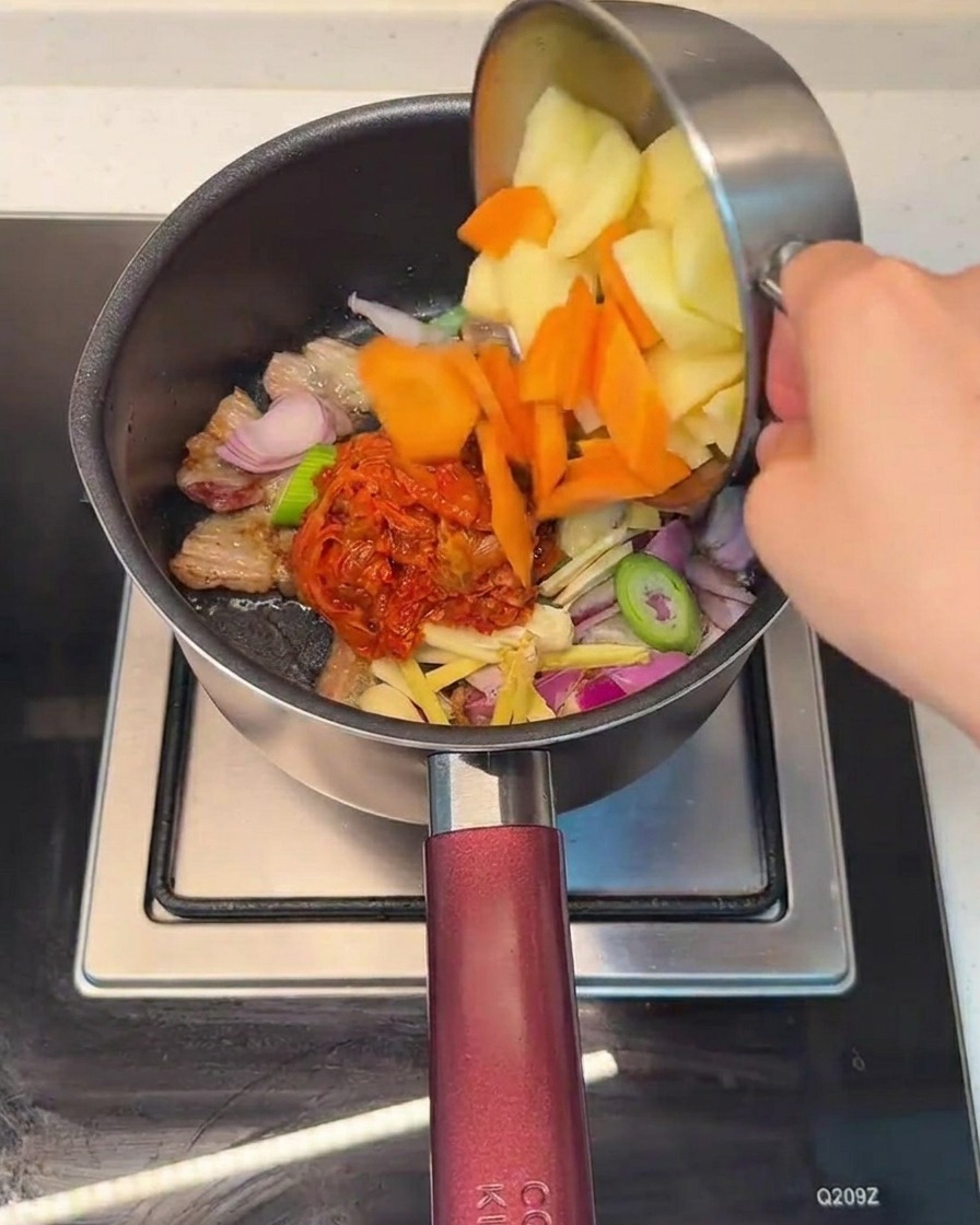 김치와 삼겹살이 볶아진 냄비에 썬 감자와 당근을 넣는 모습.