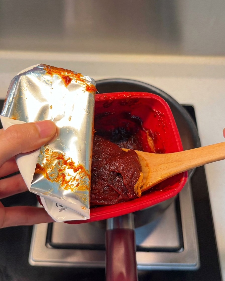 붉은 고추장을 찌개 재료 위로 한 숟가락 넣는 모습.