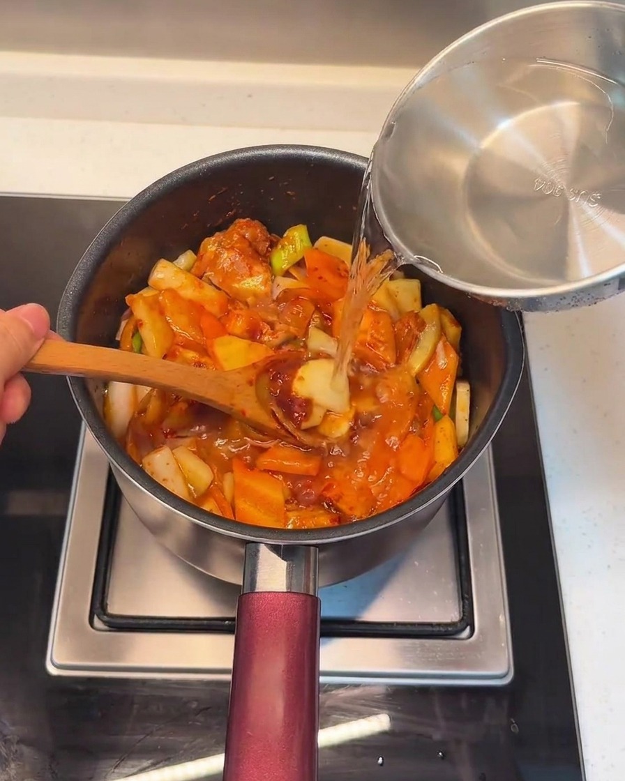 볶은 재료 위에 물을 부어 찌개를 끓이는 모습.