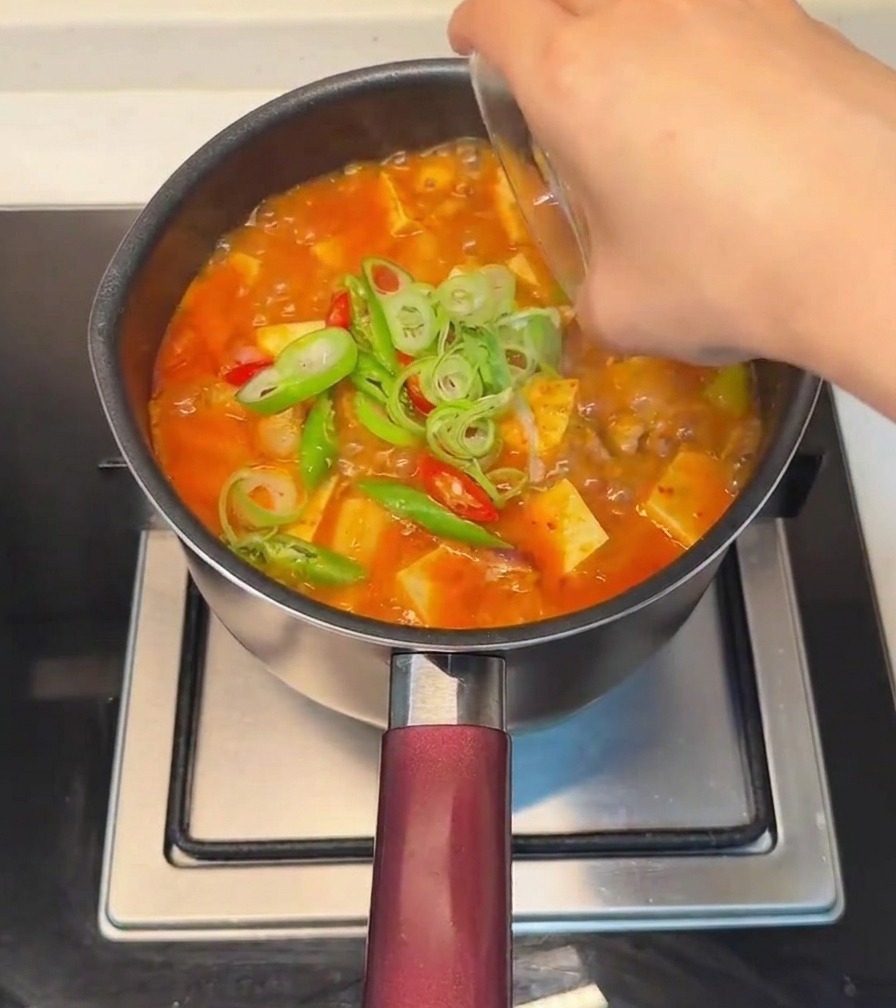 완성된 찌개 위에 대파와 고추를 고명으로 올리는 모습.