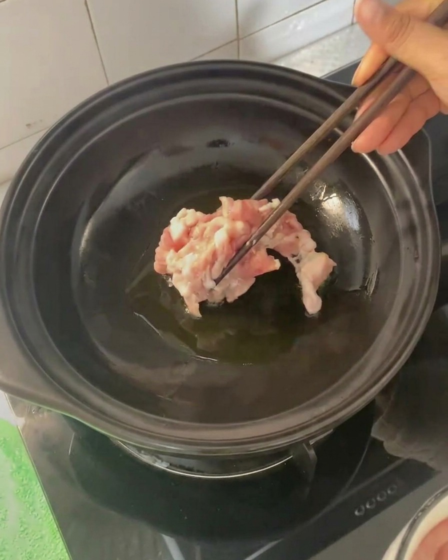 젓가락으로 달궈진 뚝배기에 삼겹살을 넣는 모습.