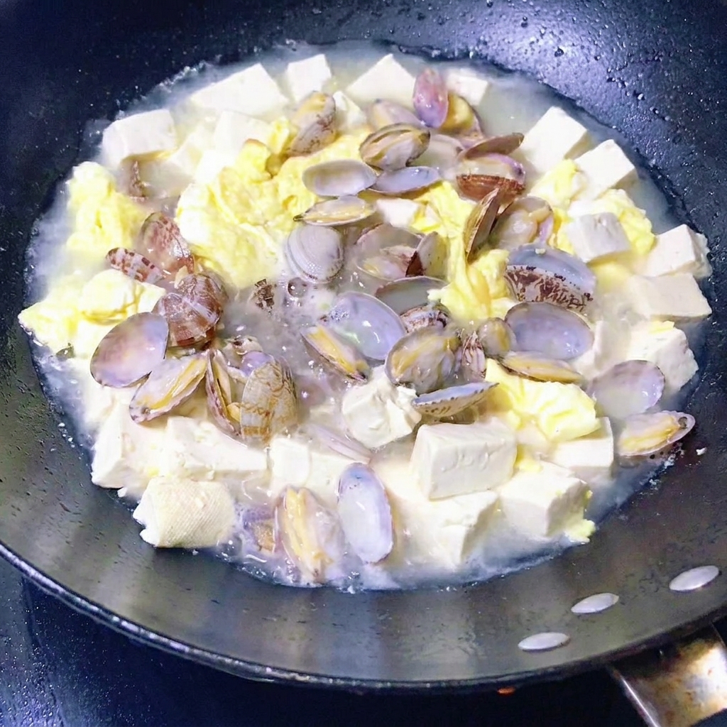 끓고 있는 바지락 두부국에 신선한 잎채소를 넣는 모습.