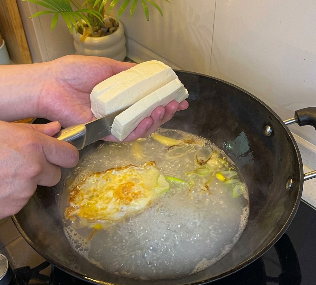 끓는 국물 속에 두부를 깍둑썰기하여 넣는 모습.
