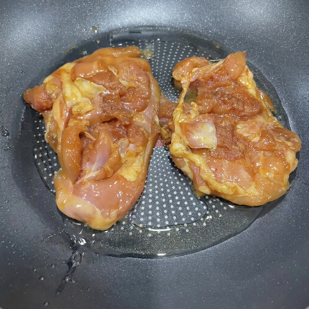달궈진 팬에 기름을 두르고 양념된 닭다리살을 굽는 모습.