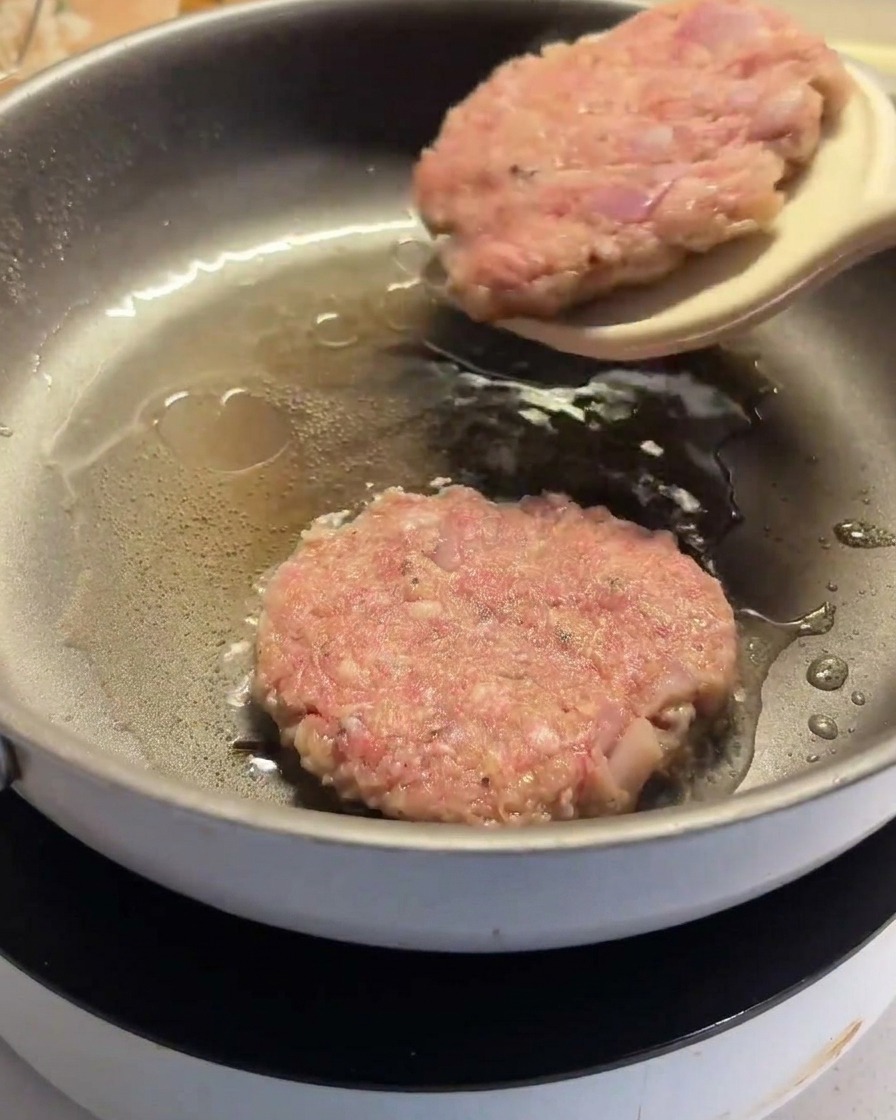 뒤집개를 사용하여 팬에서 한쪽 면이 잘 익은 함박 스테이크를 뒤집는 모습.