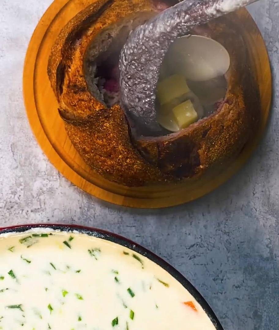 뜨거운 클램 차우더를 빵 그릇에 담고 위에 바삭한 베이컨을 올린 모습.