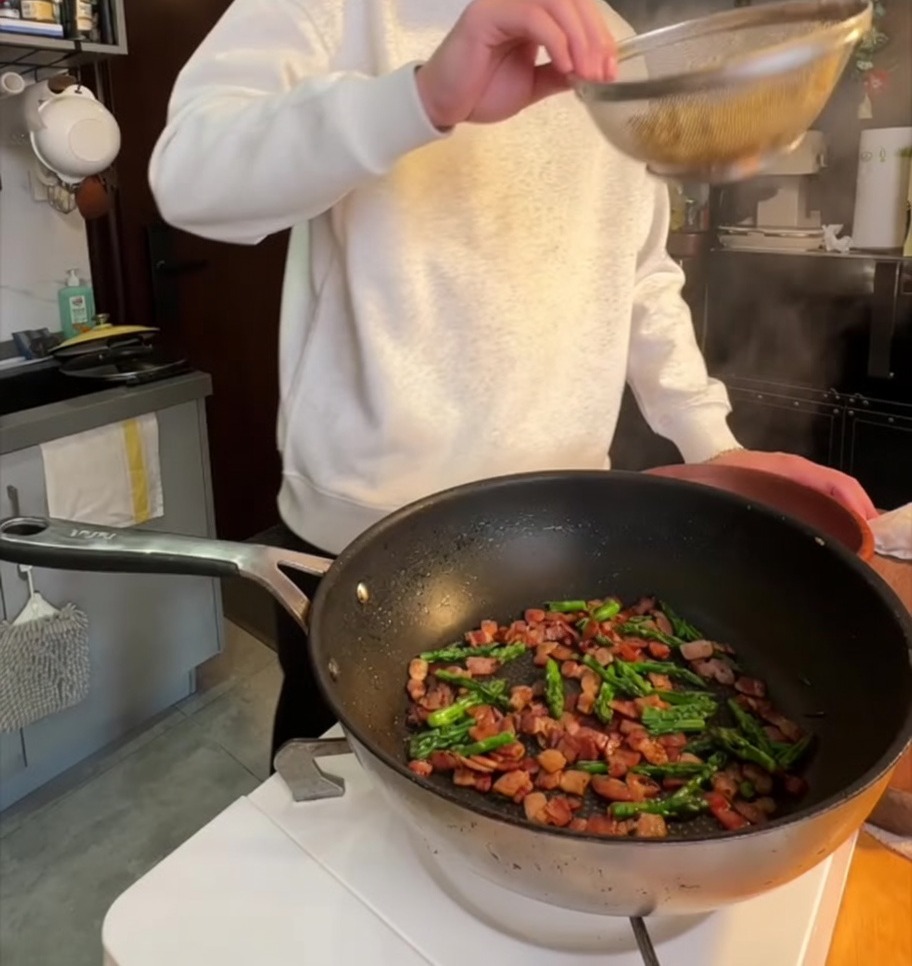 삶은 펜네 파스타를 바삭한 베이컨과 구운 아스파라거스가 있는 팬에 넣는 모습.