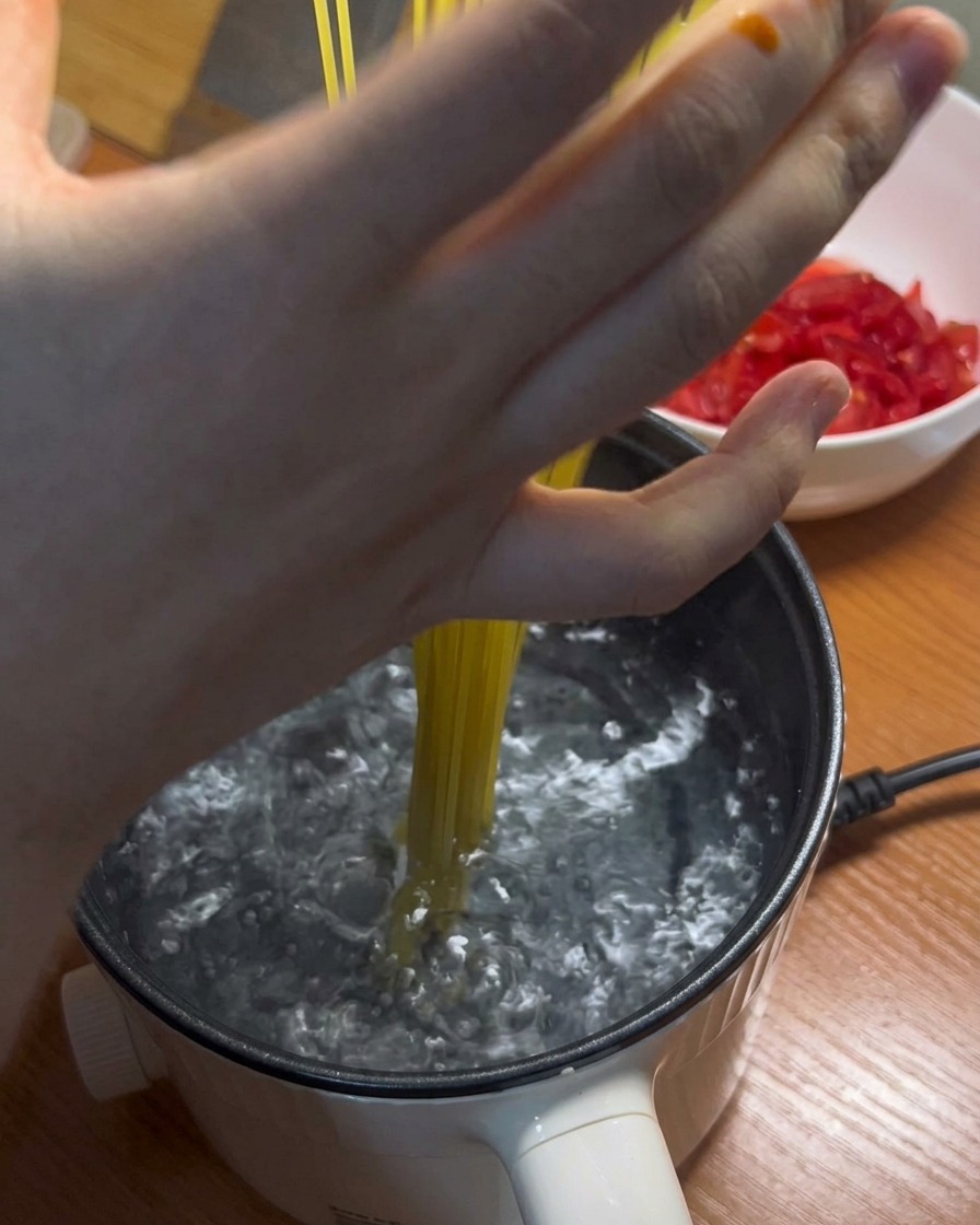 끓는 물에 긴 스파게티 면을 넣는 모습.