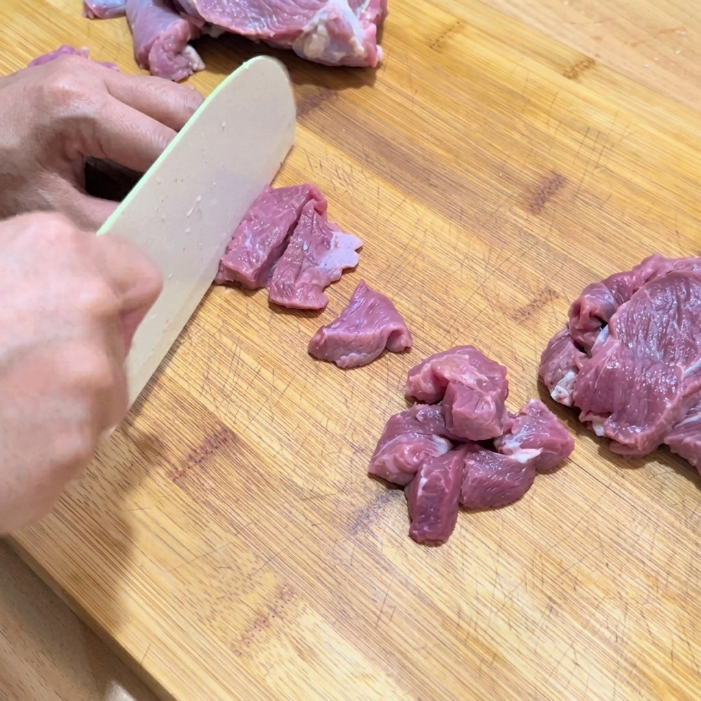 도마 위에서 생고기를 작고 균일한 큐브 모양으로 썰고 있는 모습.