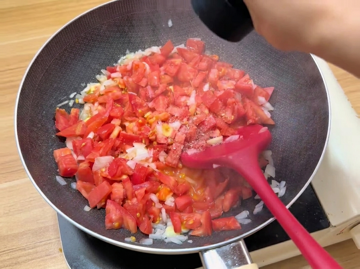 팬 안에서 토마토와 양념이 섞여 끓고 있는 모습.