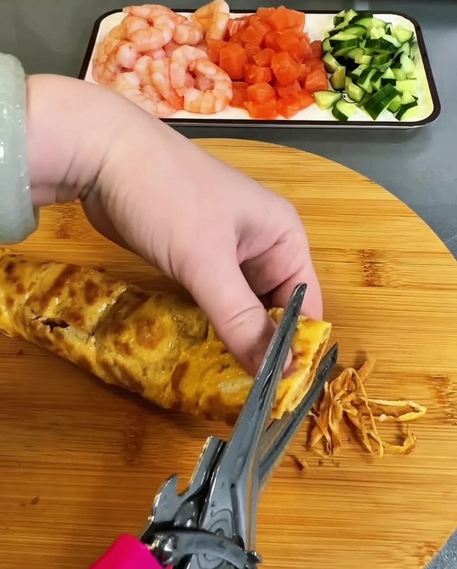부쳐진 달걀 지단을 주방 가위로 가늘게 채 써는 모습.