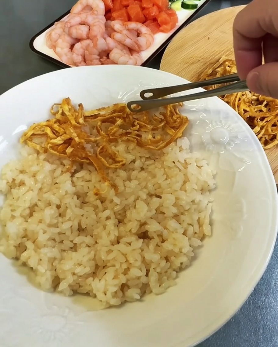 넓은 접시에 양념한 밥을 깔고 그 위에 달걀 지단과 해산물을 그룹별로 올리는 모습.