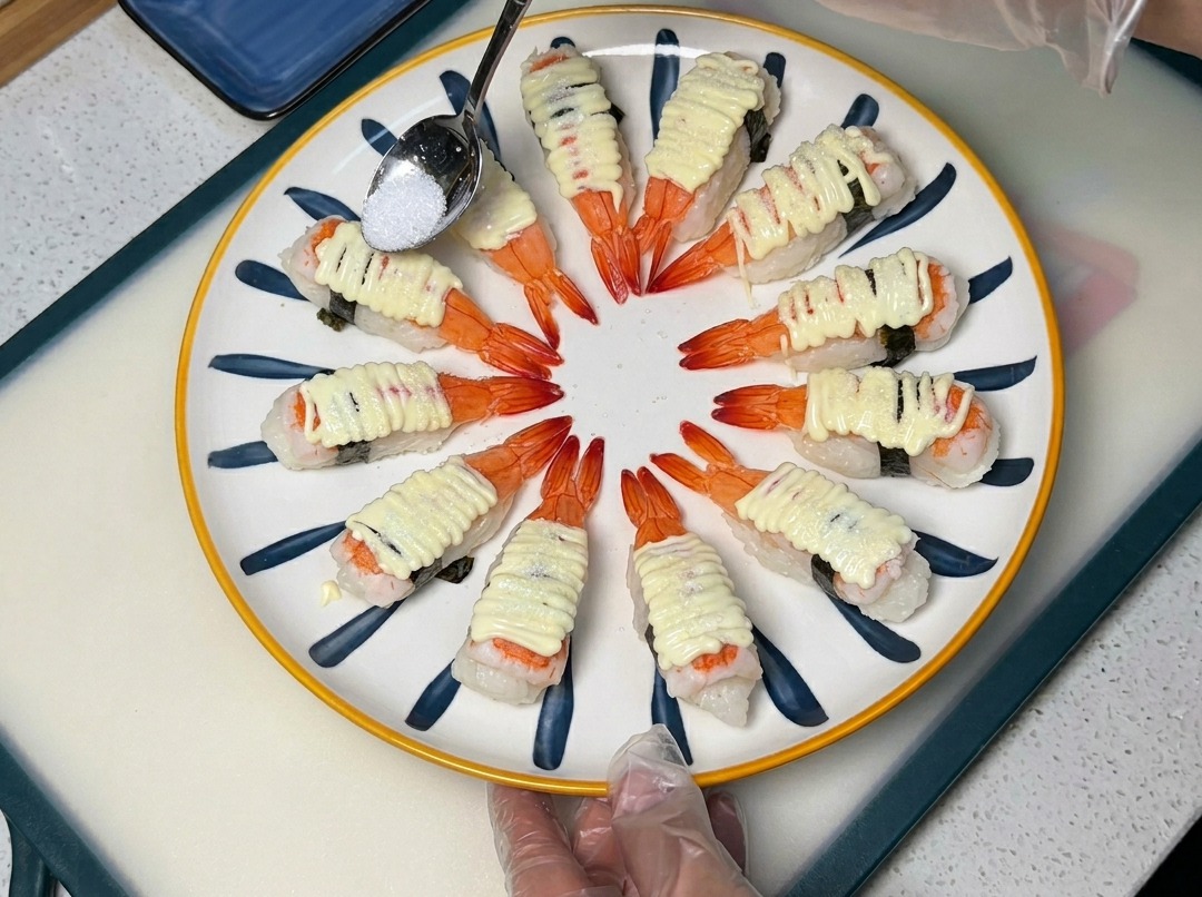 작은 숟가락으로 마요네즈가 올려진 새우 초밥 위에 설탕을 뿌리는 모습.