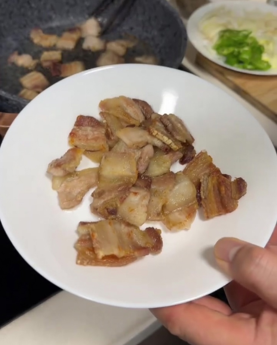 회색 팬에서 노릇하고 바삭하게 구워지고 있는 삼겹살 조각들.