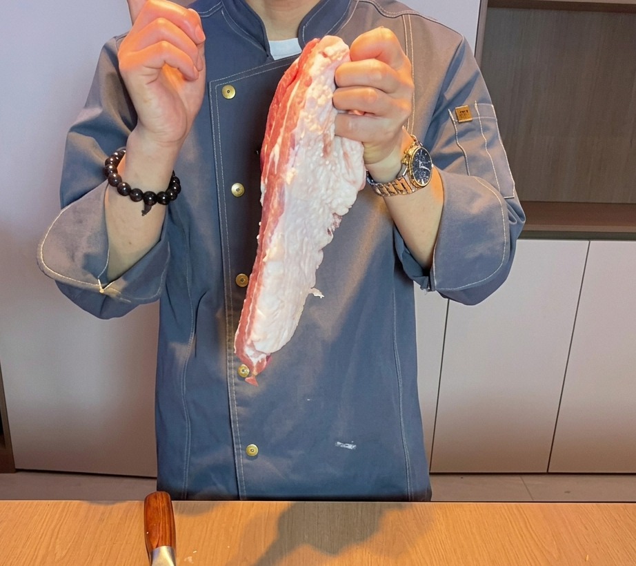 도마 위에서 신선한 생삼겹살을 두툼하게 써는 요리사의 손.