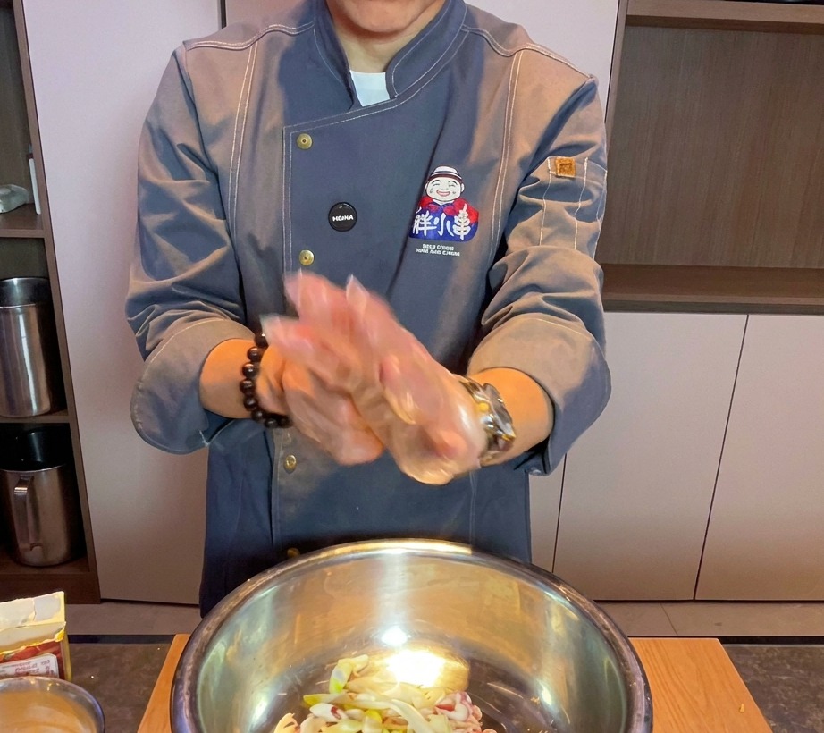 투명 장갑을 끼고 금속 볼에서 삼겹살과 향신료를 손으로 섞는 요리사.