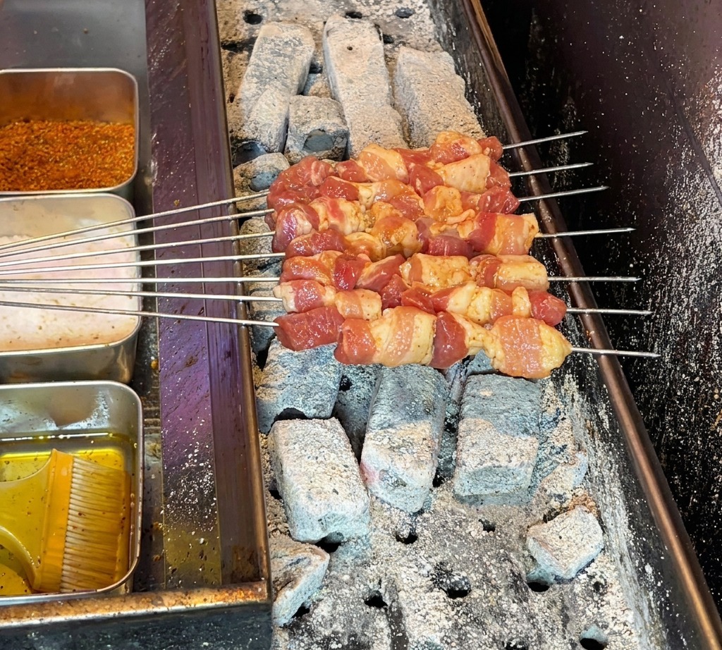 뜨거운 숯불 그릴 위에 삼겹살 꼬치를 올려 굽기 시작하는 모습.