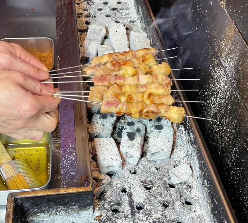 요리사가 꼬치를 조절하며 고기에 기름이 고루 배도록 굽는 모습.