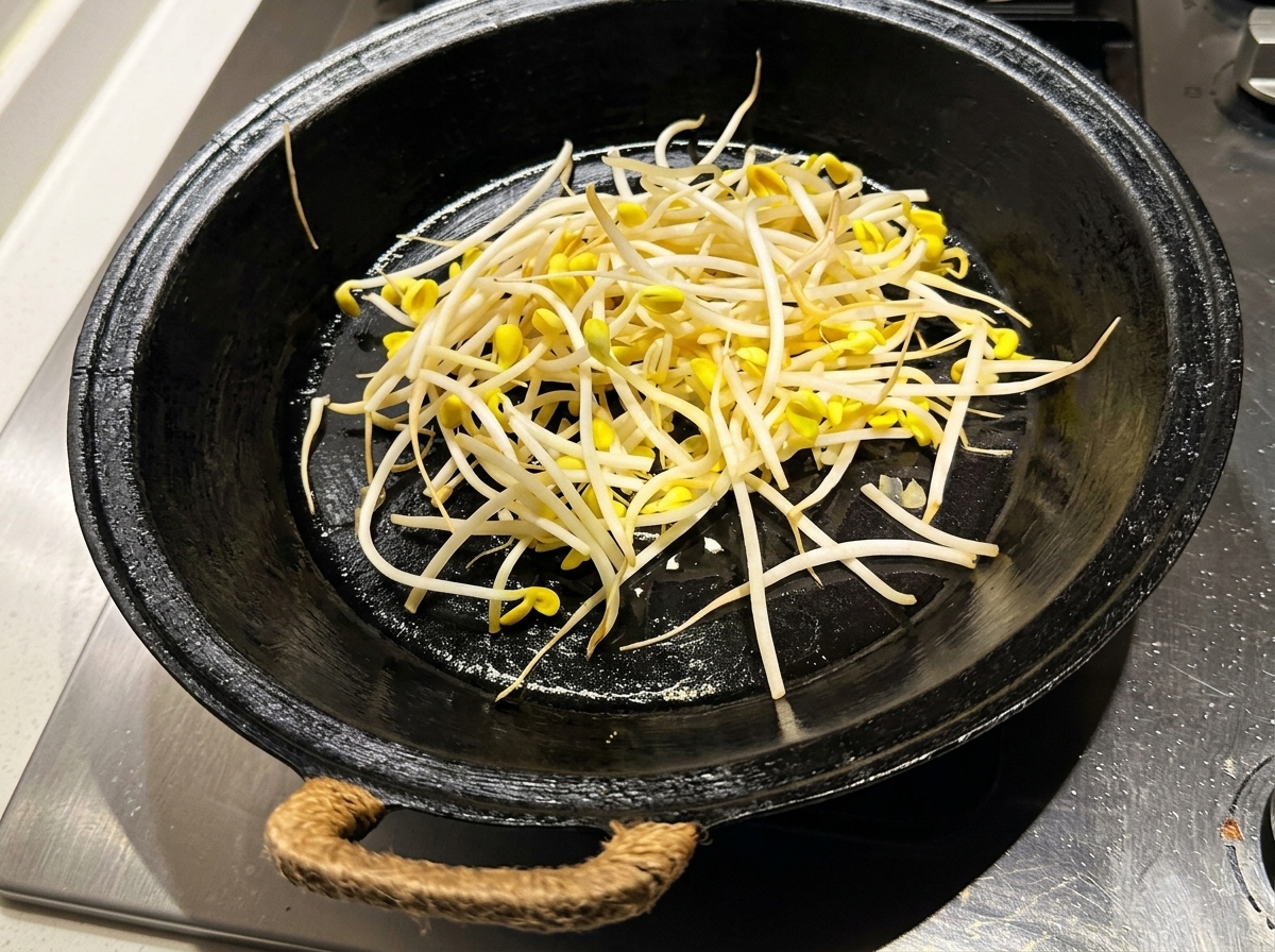 예열된 검은 팬에 씻은 콩나물을 고르게 깔아놓은 모습.