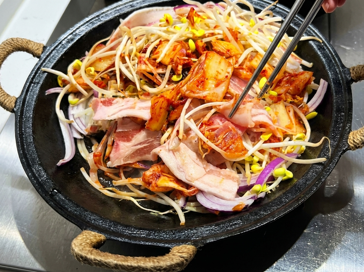 무쇠 냄비에서 집게로 재료와 양념을 섞는 모습.