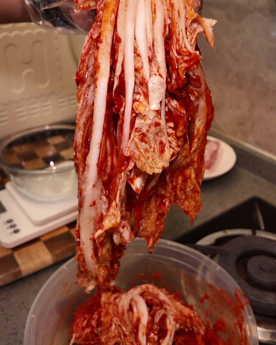 장갑을 낀 손으로 포기 김치를 들어 올리는 모습.