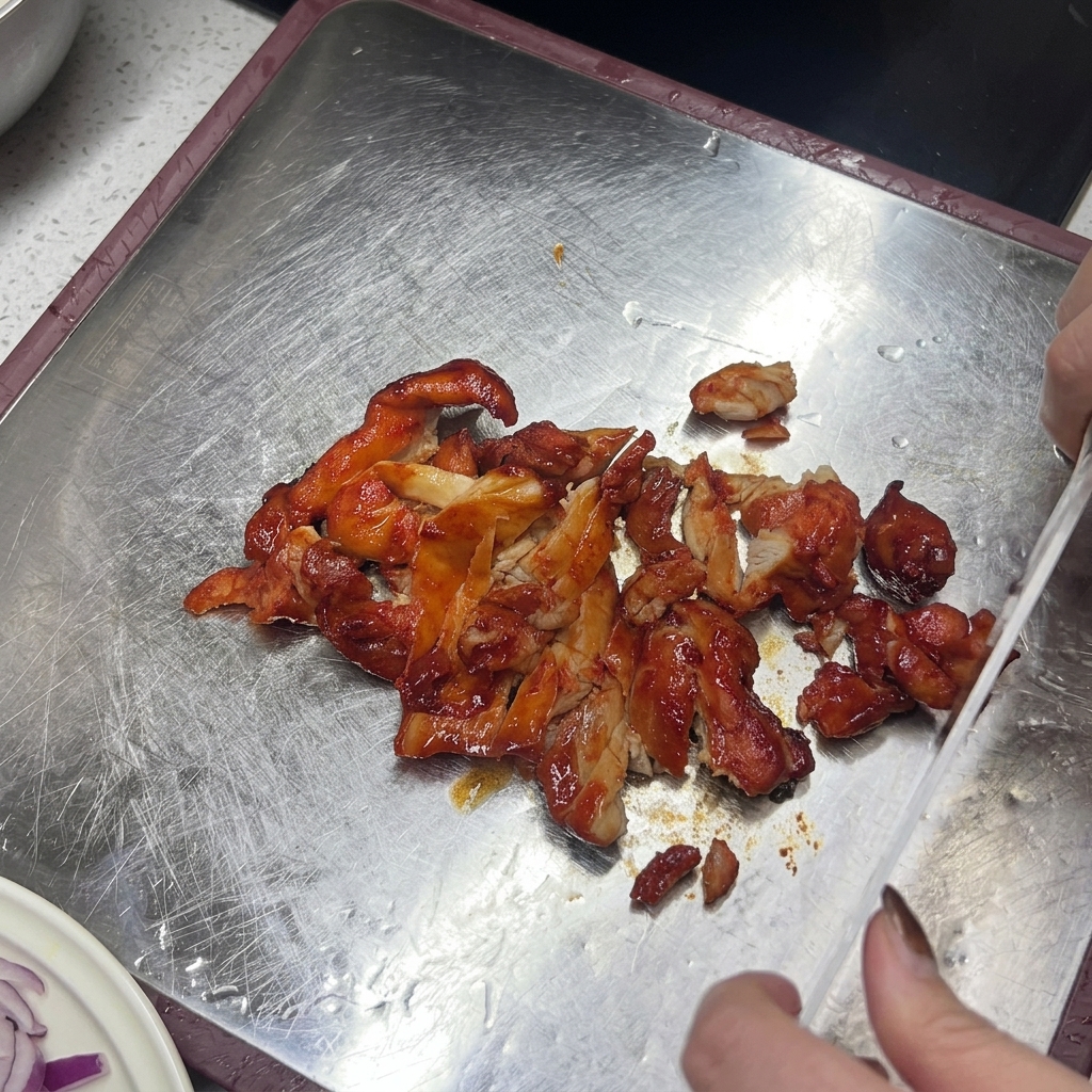 도마 위에서 노릇하게 구워진 닭고기를 칼로 써는 모습.