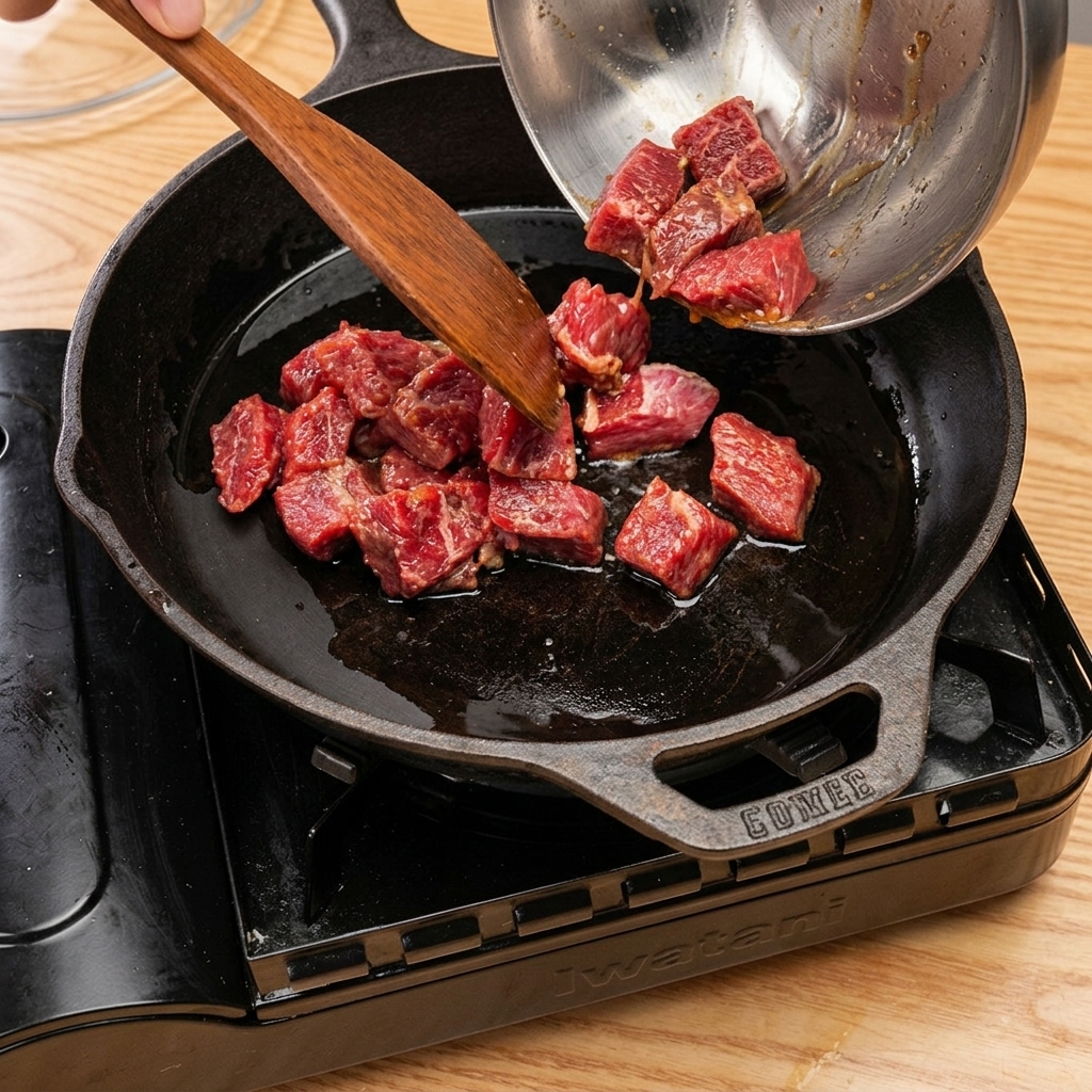 달궈진 팬에 고기를 굽고 맛술을 넣어 뚜껑을 덮는 모습.