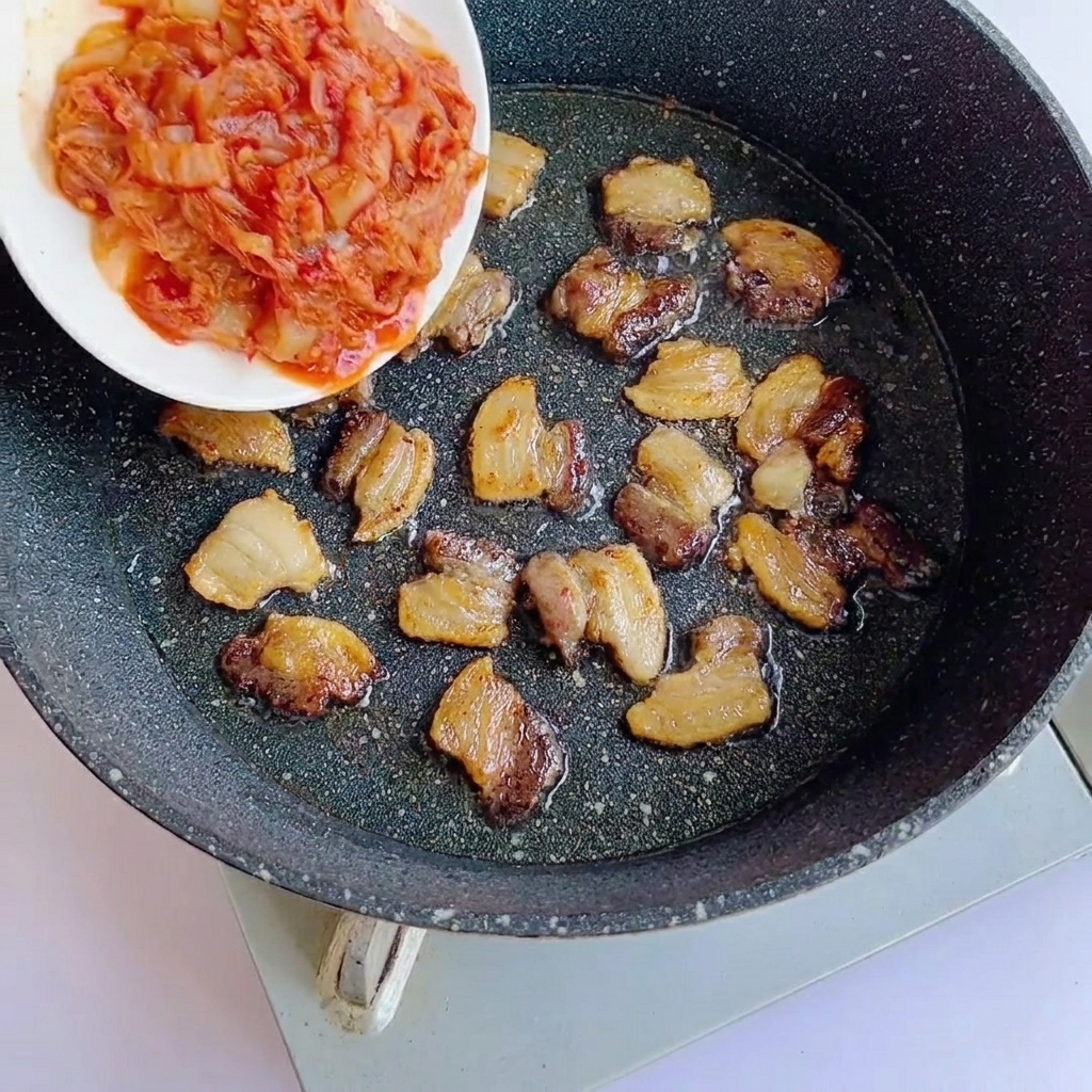 구워진 삼겹살 위에 다진 김치를 넣는 모습.