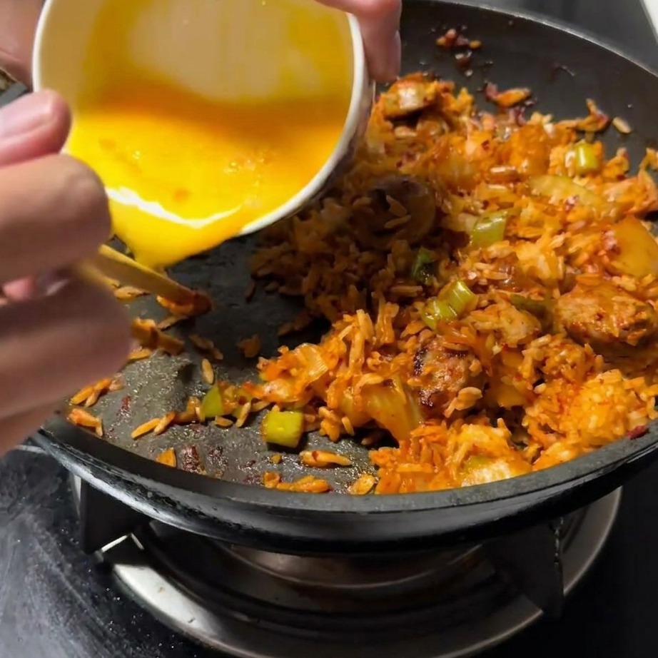 볶음밥을 한쪽으로 밀어두고 빈 공간에 푼 달걀을 붓는 모습.