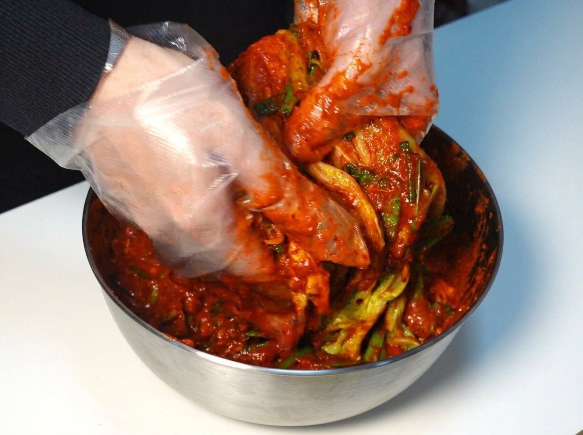 장갑을 끼고 배추 잎마다 양념을 펴 바르는 손.