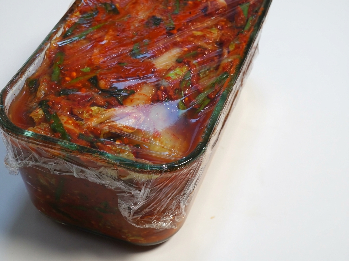 발효된 김치 용기에서 랩을 벗겨내는 모습.