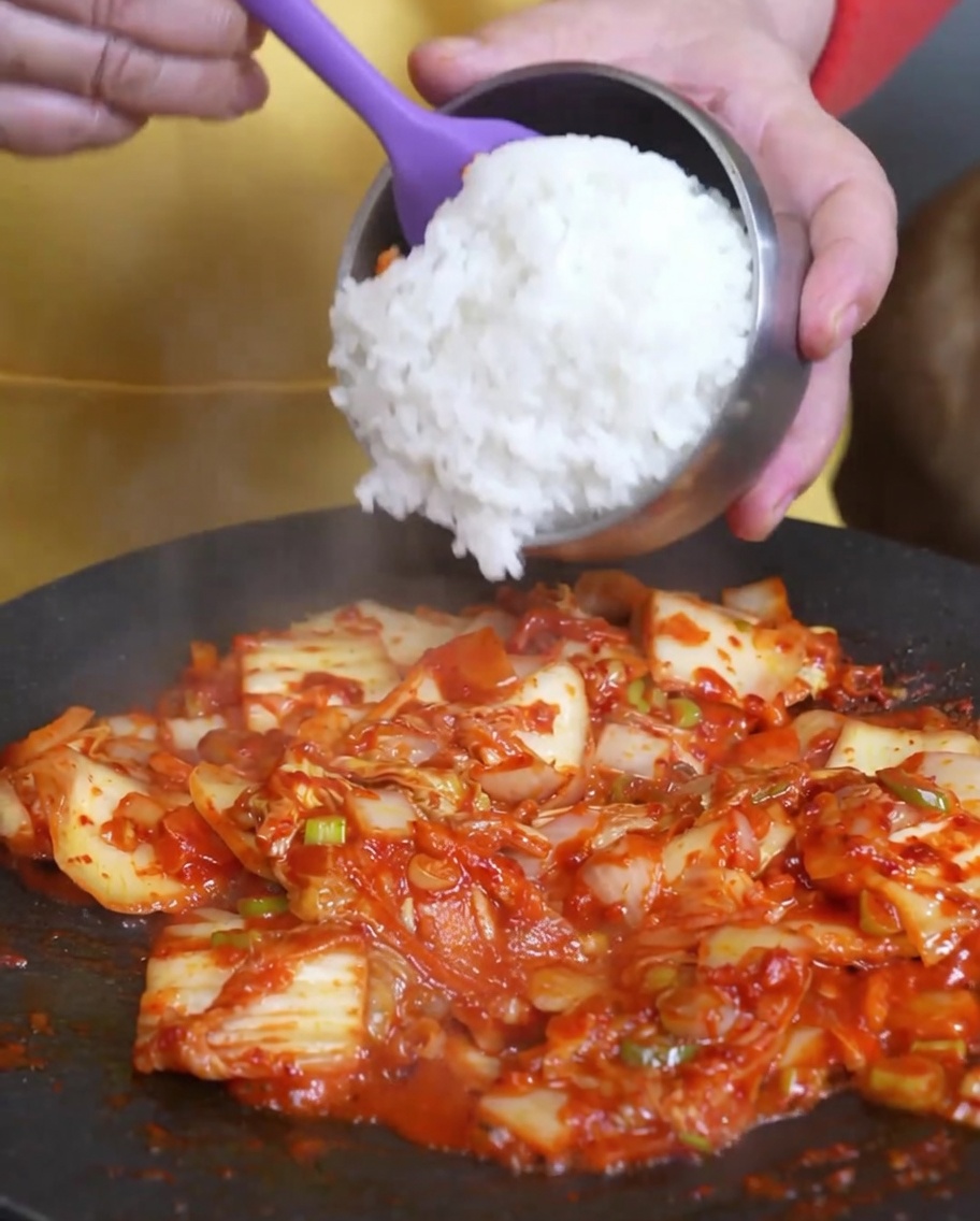 볶은 김치 위에 흰 쌀밥을 넣는 모습.