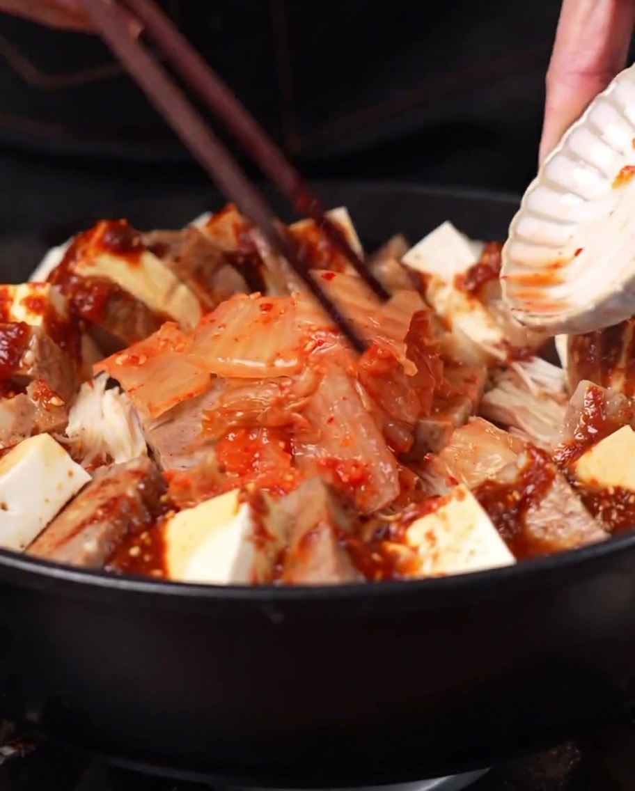 냄비 중앙에 소복하게 담긴 김치와 주변을 둘러싼 부대찌개 재료들.