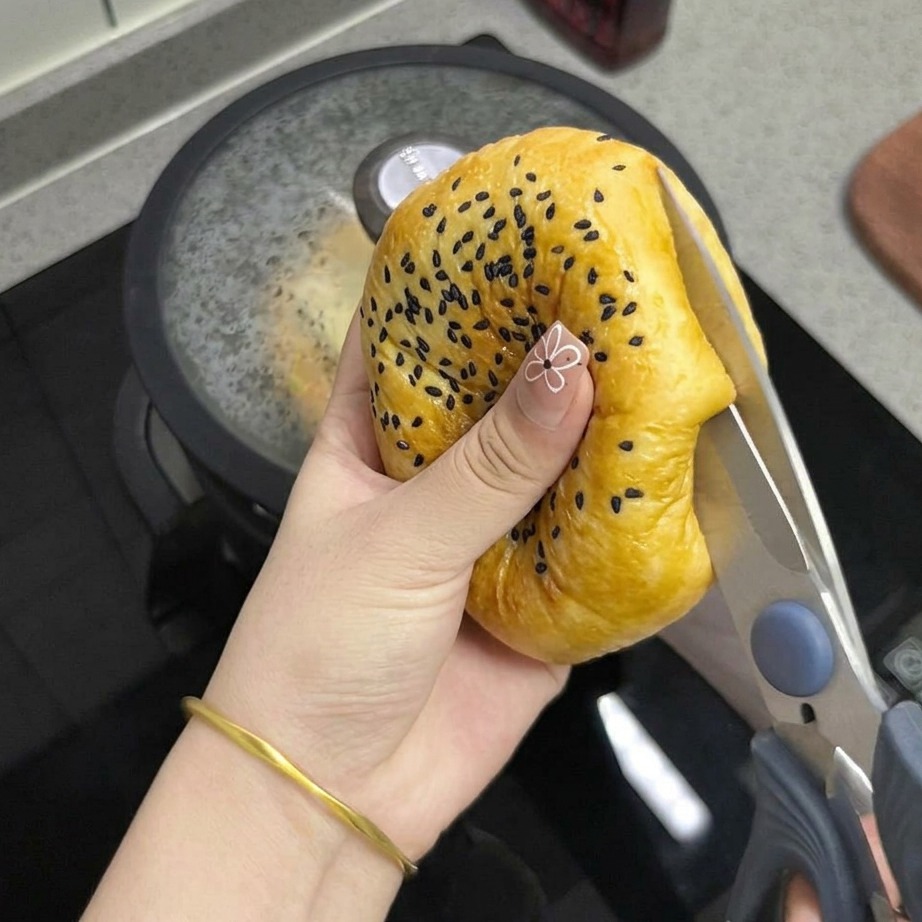 주방 가위로 구운 참깨 번을 반으로 자르는 모습.