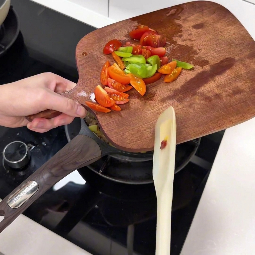 나무 도마 위에서 썬 방울토마토와 피망을 팬으로 옮기는 모습.