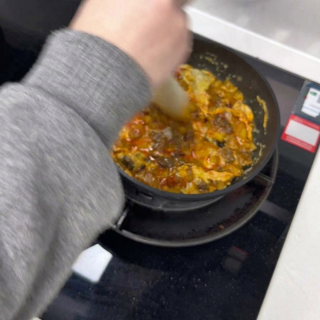 주걱을 사용해 팬 안에서 조리 중인 달걀 오믈렛을 반으로 나누는 모습.