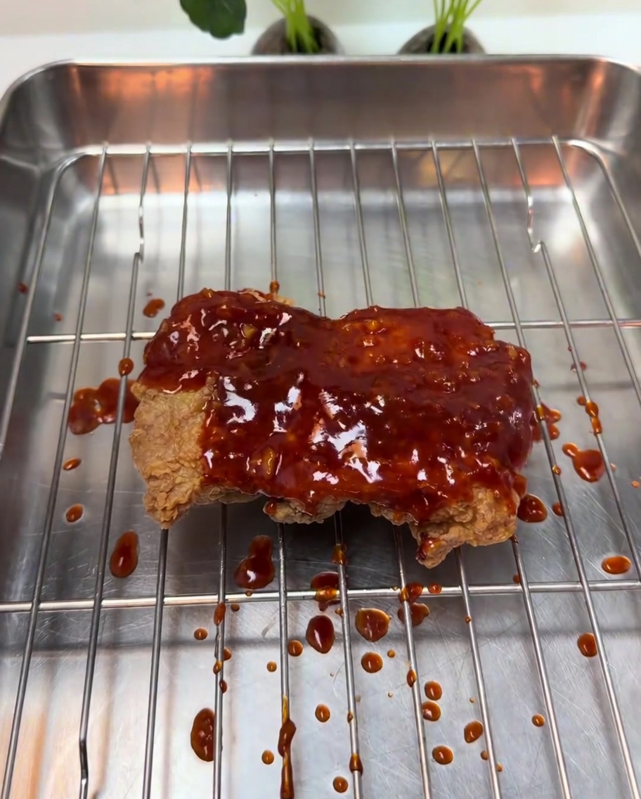 바삭한 치킨 위로 걸쭉한 붉은색 양념이 뿌려지는 모습.