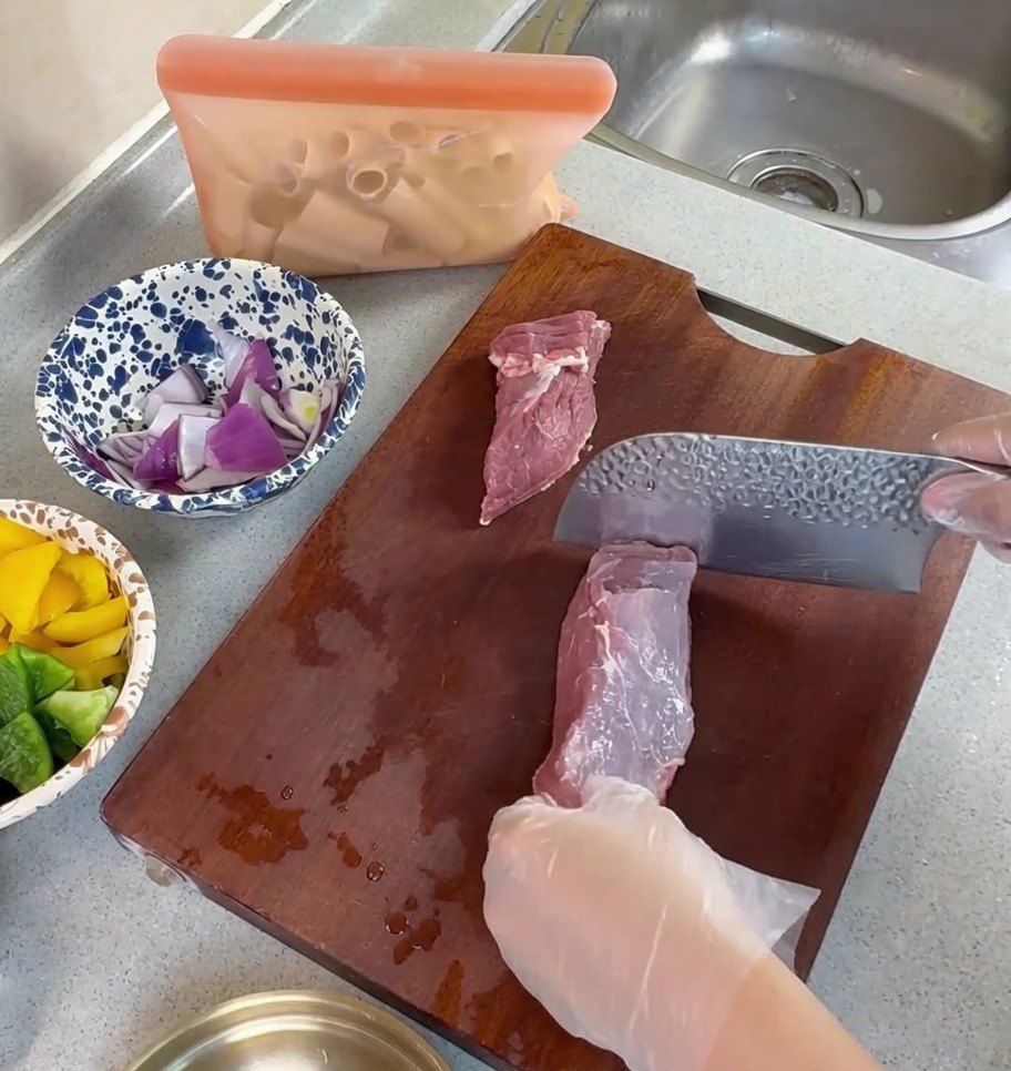 도마 위에서 중식 칼을 사용하여 생 돼지고기를 얇게 써는 모습.