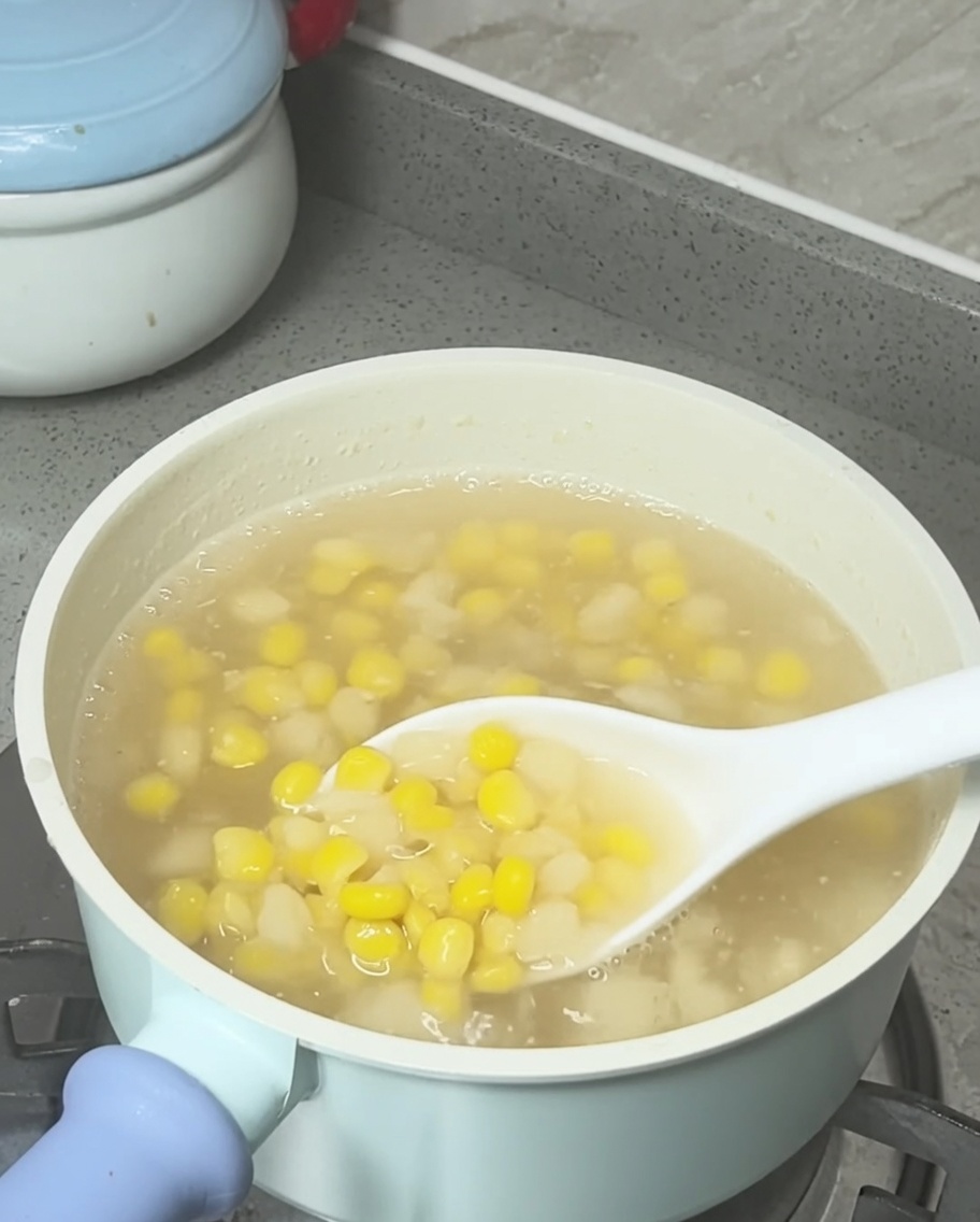 완성된 옥수수 물밤 수프 냄비 위에 코코넛 밀크를 뿌리는 모습.