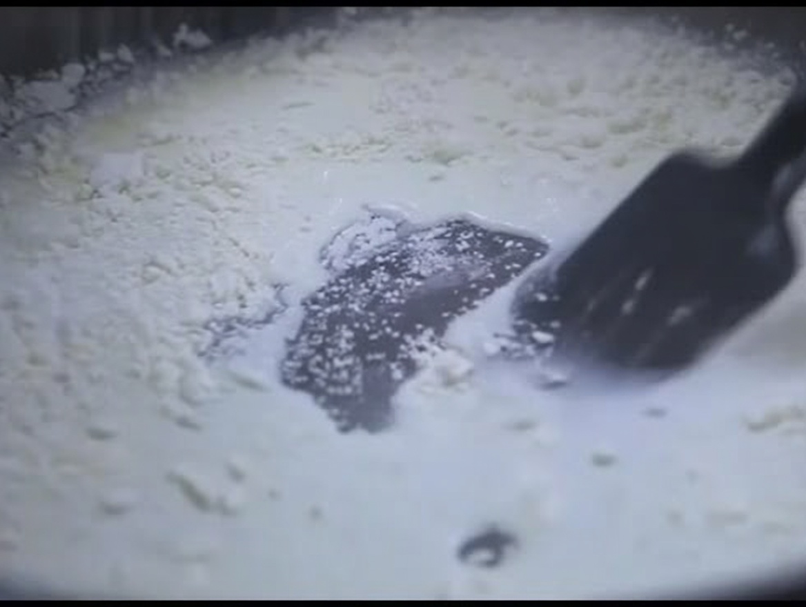 검은색 실리콘 주걱으로 팬 속의 걸쭉한 우유 밀가루 혼합물을 젓는 모습.
