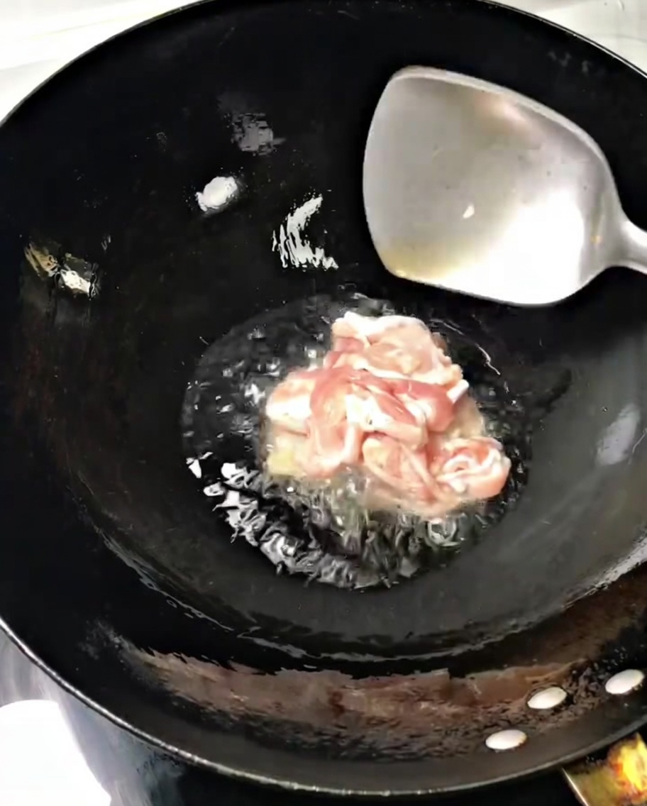 달궈진 웍에 기름을 두르고 돼지고기 슬라이스를 금속 뒤집개로 볶는 모습입니다.