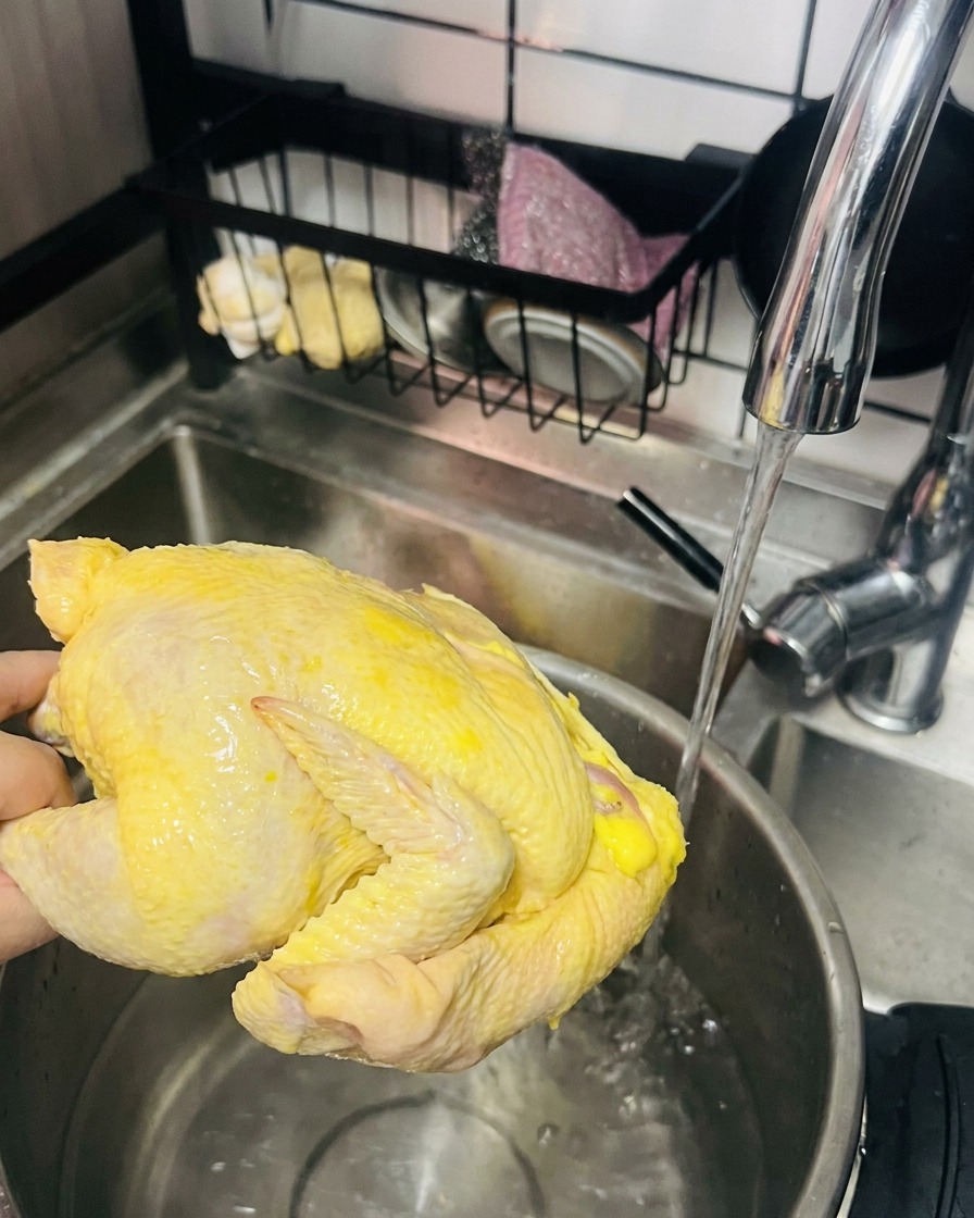 흐르는 물에 씻어 냄비에 넣을 준비가 된 노란 닭 한 마리.