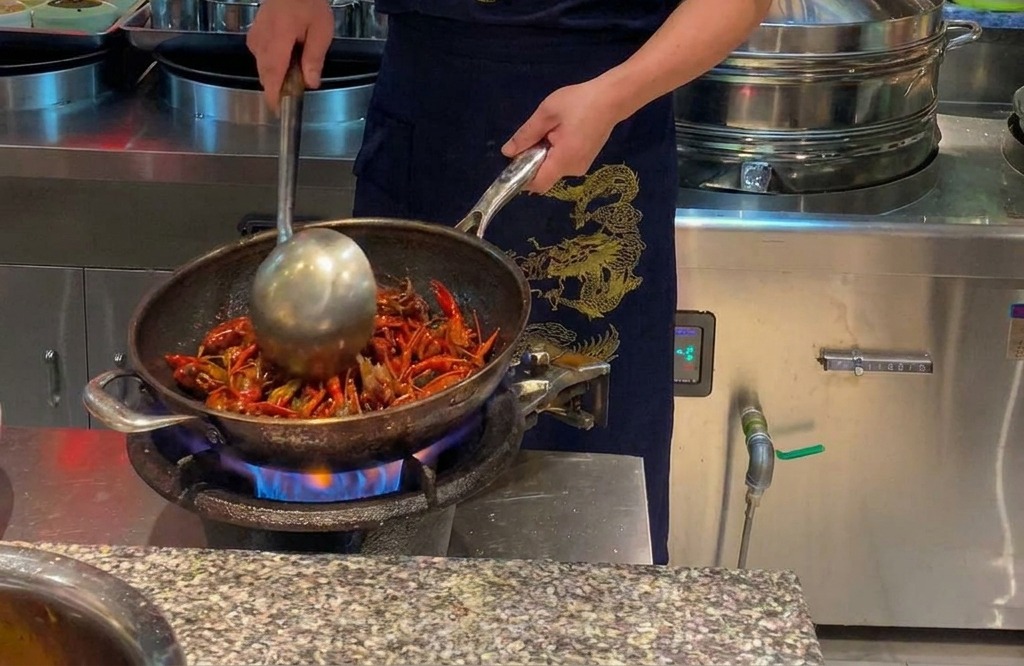 불 위에서 큰 웍에 담긴 선명한 붉은색의 가재를 볶고 있는 셰프.