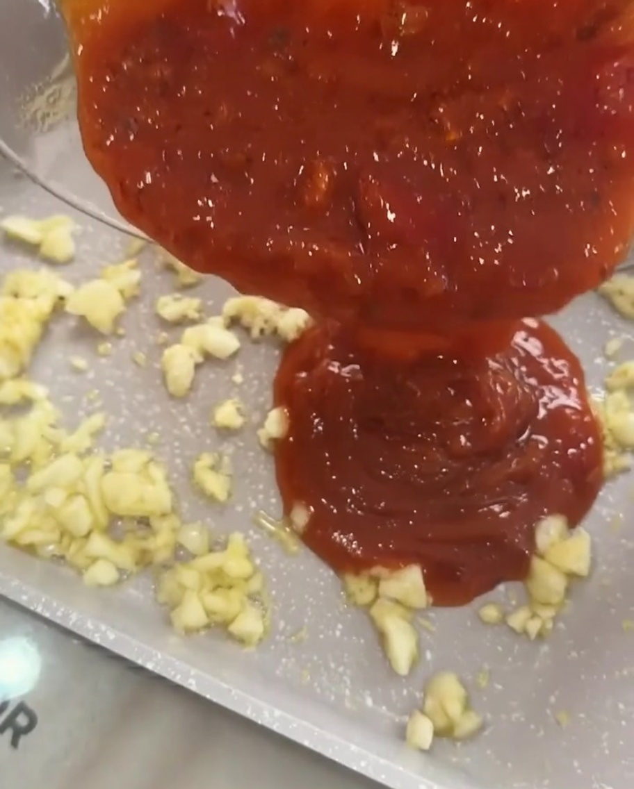 볶아진 마늘 위로 토마토 미트 소스를 붓는 모습.