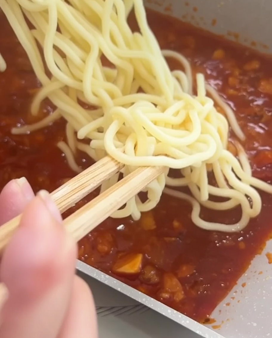 삶아진 스파게티 면을 팬에서 소스와 함께 젓가락으로 섞는 모습.
