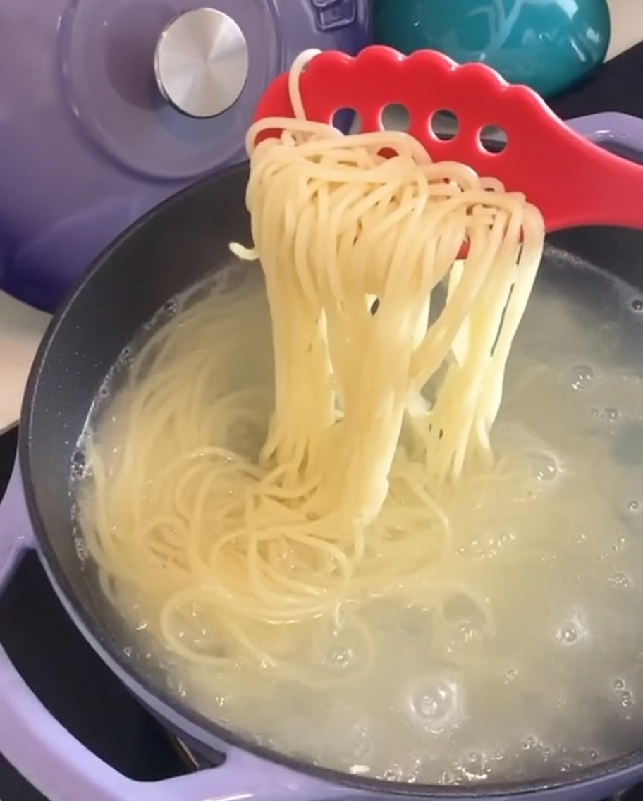 빨간색 파스타 포크로 냄비에서 삶은 스파게티 면을 건져내는 모습.