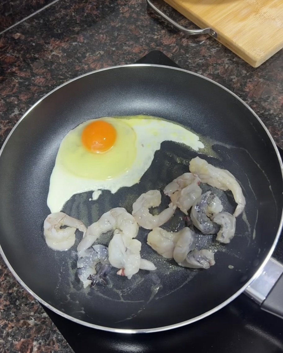 프라이 중인 달걀 옆에서 새우가 갈색으로 익어가는 모습.