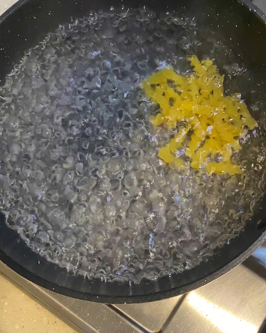펄펄 끓는 물이 담긴 어두운 냄비에 노란 푸실리 파스타를 넣는 모습.