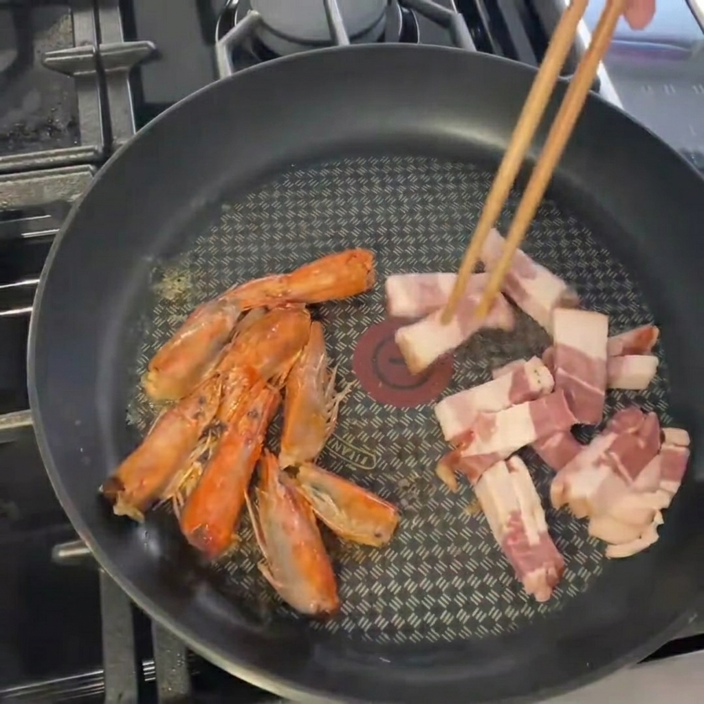새우 머리를 볶던 팬에 잘게 썬 베이컨을 넣는 모습.